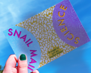 A postcard that says "snail mail science" being held up against a blue sky
