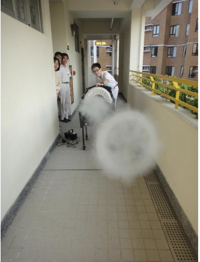 A photo showing four people playing air cannon dodge ball. The air cannon was made by following the game's instructions. In the photo they have just released the air cannon and there is a puff of smoke.